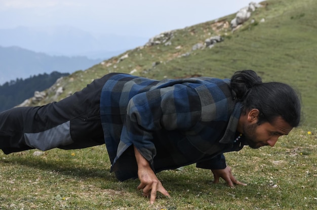 Foto ein hübscher, langhaariger indischer junger mann macht push-ups mit drei fingern auf dem gipfel des berges