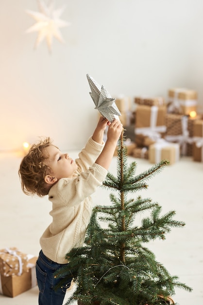 Ein hübscher lockiger kleiner Junge schmückte einen Weihnachtsbaum