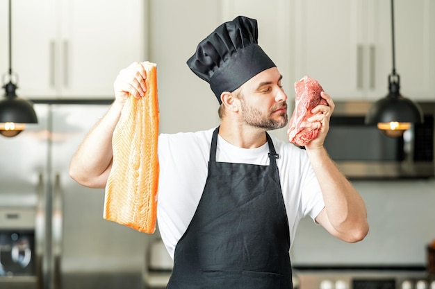 Ein hübscher Mann kocht Fisch und Fleisch, Lachs und Rindfleisch in der Küche. Porträt eines beiläufigen Mannes, der in der Kücherei kocht.