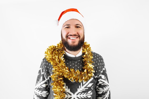 Ein hübscher Mann mit einem Bart in einem Weihnachtspullover, der eine Weihnachtsmannmütze auf einem weißen Hintergrund trägt