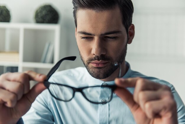 Ein hübscher, nachdenklicher Geschäftsmann schaut auf seine Brille und denkt nach, während er im Büro arbeitet