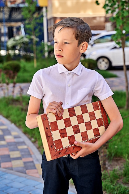 Foto ein hübscher schuljunge in einem weißen hemd mit einem schachbrett.