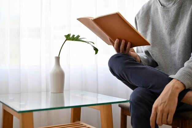 Ein hübscher und lässiger junger asiatischer Mann, der ein Buch liest, während er sich im Café entspannt