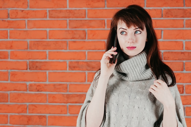 Ein hübsches Mädchen, das durch Mobiltelefon, überraschte Augen, im grauen Pullover spricht