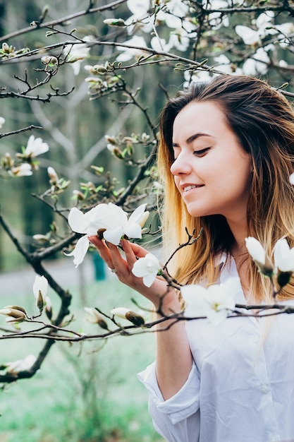 Ein hübsches Mädchen in einem Garten genießt blühende Magnolienbäume