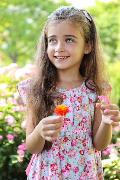 ein hübsches Mädchen mit braunen Haaren und hellgrünen Augen, glücklich und lächelnd mit zwei Blumen