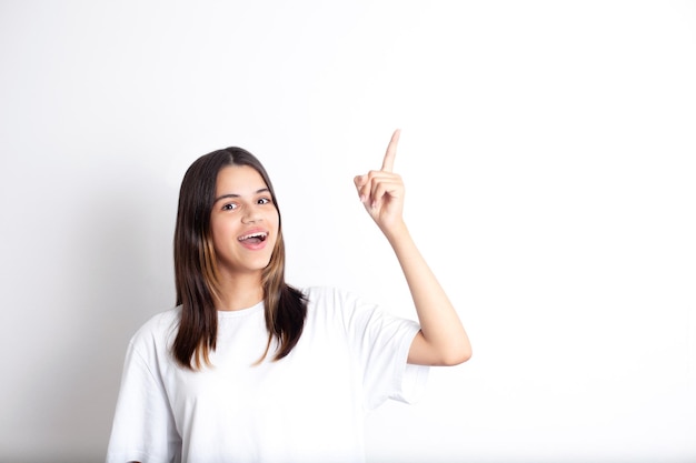 Ein hübsches Teenager-Mädchen mit dunklen Haaren mit einem Lächeln zeigt mit dem Finger nach oben Ein Platz für Text Weißer Hintergrund Positive Freude Spaß