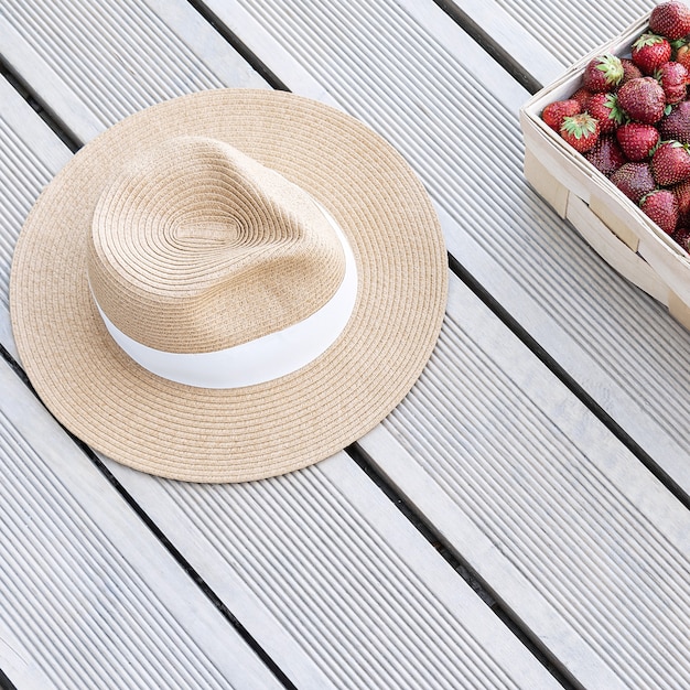 Ein Hut und frische Erdbeeren liegen in einem Korb auf Terrassenbrettern