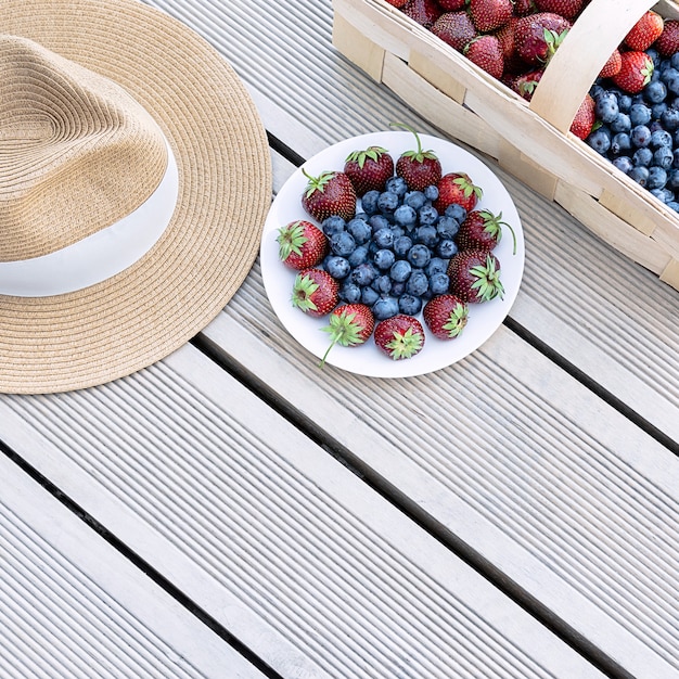 Ein Hut und frische Erdbeeren und Blaubeeren liegen in einem Korb