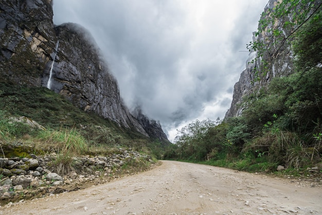 Foto ein idyllischer weg schlängelt sich durch zerklüftete berge, geschmückt mit einem wasserfall und üppigem grün. inspirierende bilder für natürliche landschaften