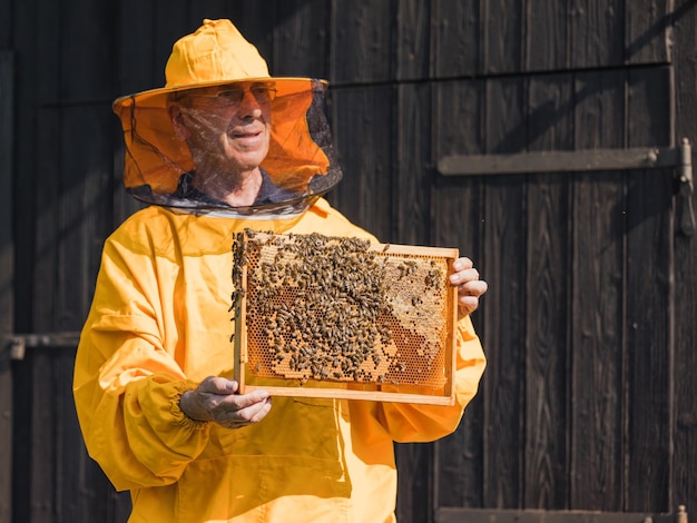 Foto ein imker in schutzausrüstung hält einen bienenstockrahmen mit honigstock