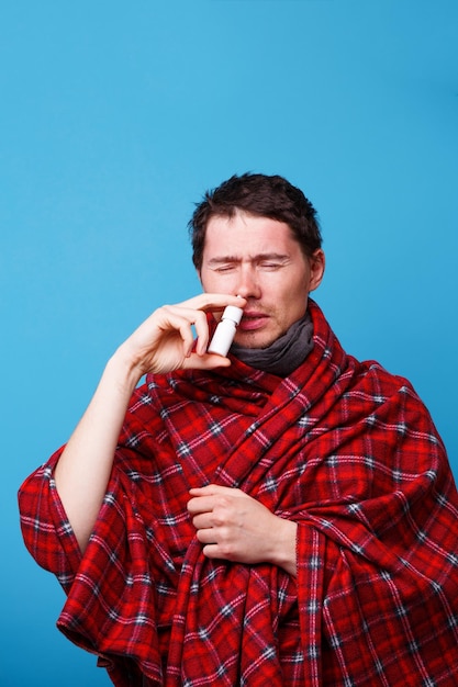 Ein in eine Decke gehüllter kranker Mann steht und benutzt Nasenspray