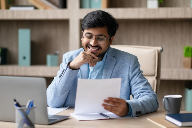 Ein indischer Geschäftsmann hält und liest Dokumente in Innenräumen.