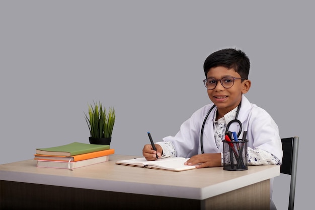Ein indischer Junge im Alter von 7 bis 8 Jahren, der eine Arztschürze mit Stethoskop trägt und ein Rezept schreibt