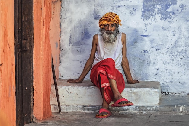 Ein indischer Mann mit grauem Bart sitzt auf einer Stufe in der Nähe des Hauses Varanasi Indien 09032023