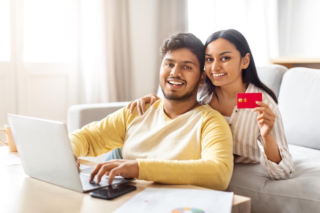 Ein indischer Mann und eine indische Frau sitzen auf der Couch und halten eine rote Kreditkarte in der Hand