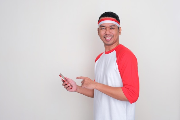 Ein indonesischer Mann lächelt und zeigt auf sein Handy, das er hält