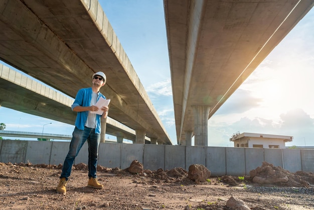 Ein Ingenieur hält Baupläne in der Hand, um den Baufortschritt auf der Straßenbaustelle zu überprüfen