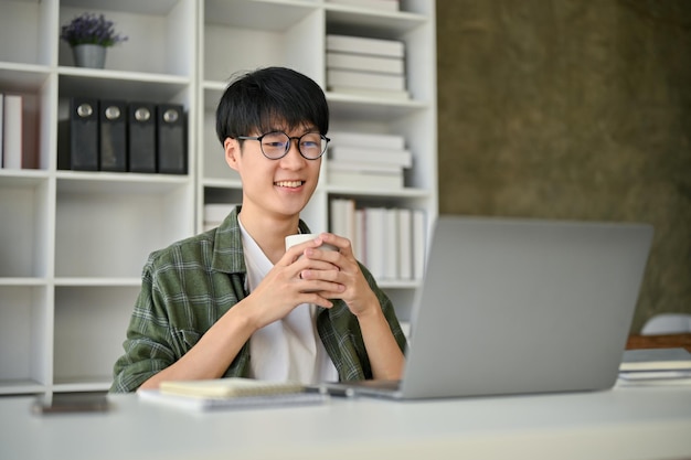 Ein intelligenter asiatischer männlicher Büroangestellter mit Brille, der etwas auf seinem Laptop-Bildschirm liest