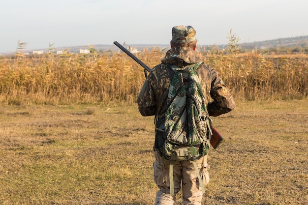 Ein Jäger mit einer Waffe in der Hand in Jagdkleidung im Herbstwald auf der Suche nach einer Trophäe