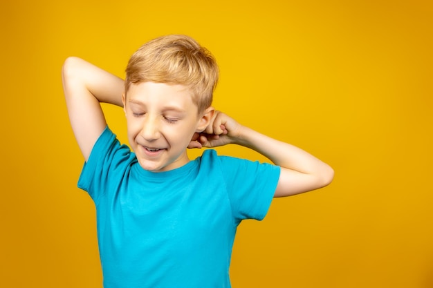 Ein Junge auf gelbem Hintergrund in einem blauen T-Shirt streckt sich und schließt die Augen