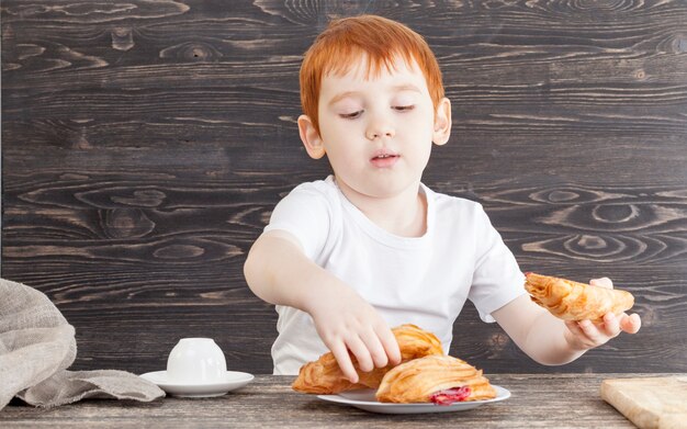 Ein Junge beim Essen eines Desserts aus einem weißen Brötchen mit Weizenpuff und roter Kirschmarmelade auf einem schwarzen