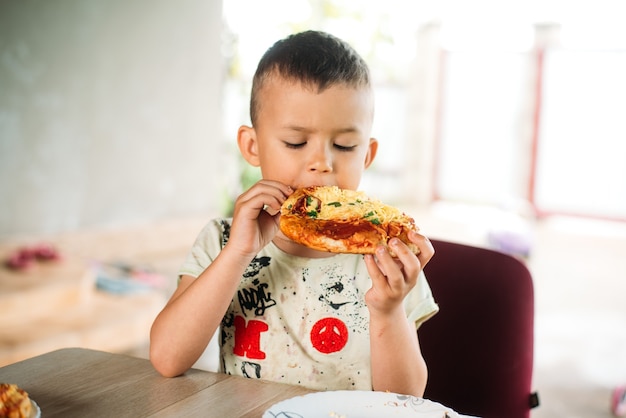 Ein Junge, ein Kind auf der Straße isst eine Minipizza sehr appetitlich