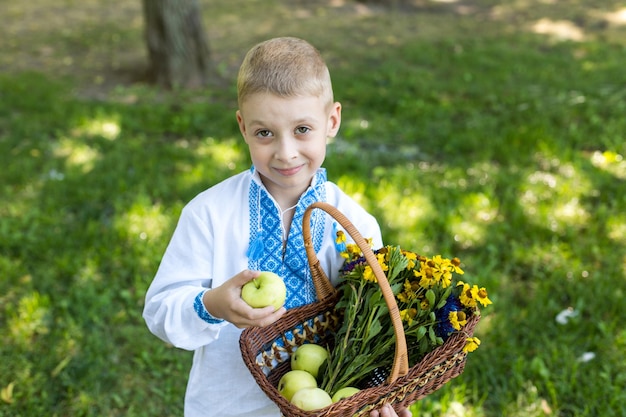 Ein Junge hält einen Korb voller Äpfel und einen Blumenstrauß.