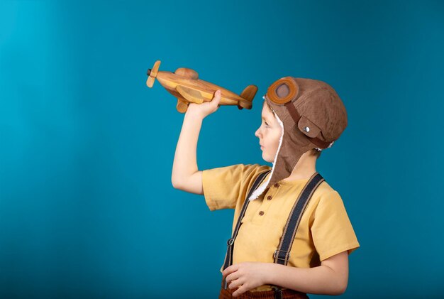 Ein Junge im Grundschulalter hält auf blauem Hintergrund ein Spielzeug-Holzflugzeug in den Händen