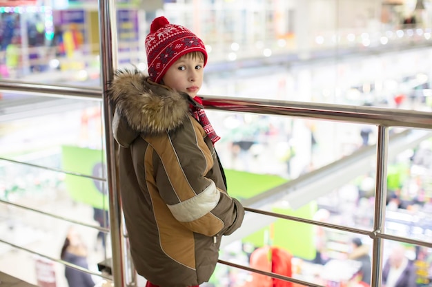 Ein Junge im Grundschulalter in Winterkleidung steht drinnen an einem Metallhandlauf