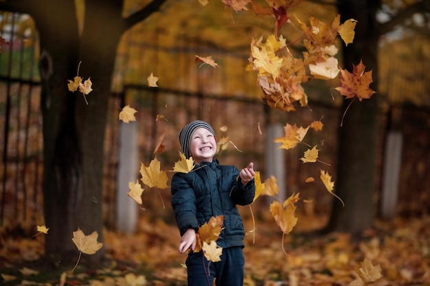 Ein Junge im Herbstwald wirft Blätter und freut sich