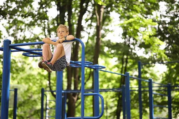 Ein Junge im Park treibt Sport, klettert auf die Klimmzugstange und zieht die Beine an