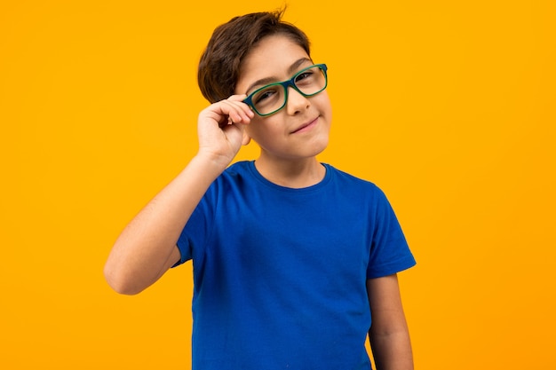 Ein Junge in einem blauen T-Shirt hält eine Brille mit der Hand und schaut misstrauisch in leuchtendem Gelb in die Kamera