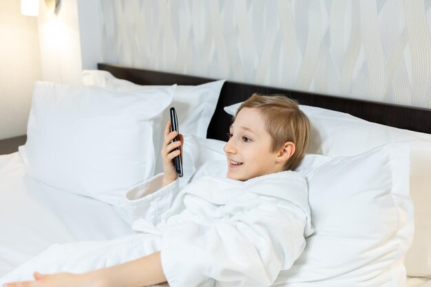 Ein Junge in einem Hotelzimmer liegt auf dem Bett, hält ein Telefon vor sich und telefoniert über die Freisprecheinrichtung