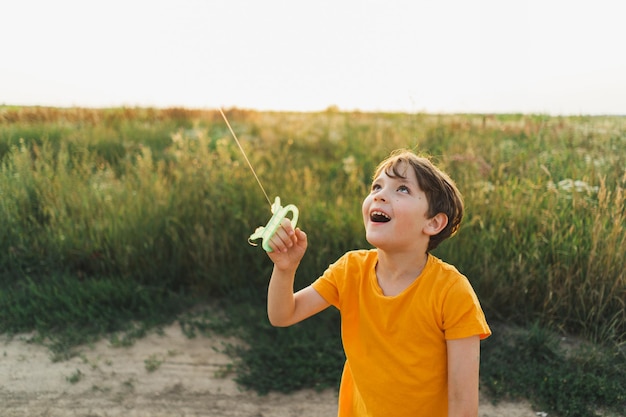 Ein Junge in einem orangefarbenen T-Shirt fliegt einen Drachen in der Natur, ein glückliches Kind