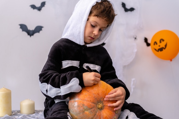 Ein Junge in einem Skelettkostüm malt einen Kürbis glückliches Halloween