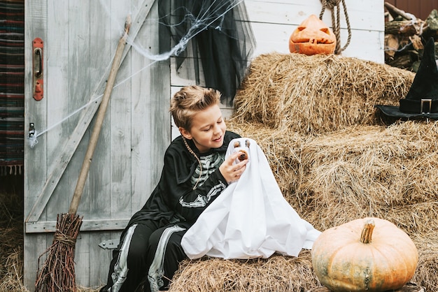 Ein Junge in einem Skelettkostüm mit einem Hund in einem Geisterkostüm auf der Veranda eines Hauses, das dekoriert wurde, um eine Halloween-Party zu feiern