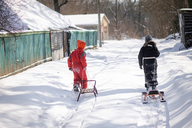 Ein Junge in einem Skianzug auf einem Schneeberg mit einem Schlitten. Das Kind fährt einen Schlittenroller. Aktive Spiele auf der Straße. Gesunder Lebensstil