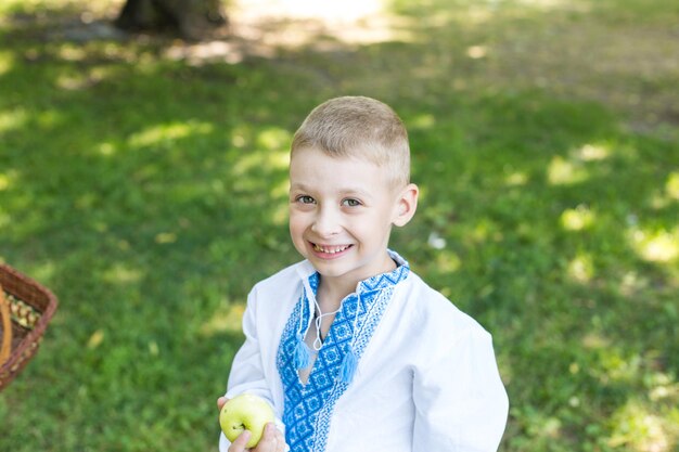 Ein Junge in einem weißen Hemd mit blauen Mustern hält einen Apfel in der Hand.