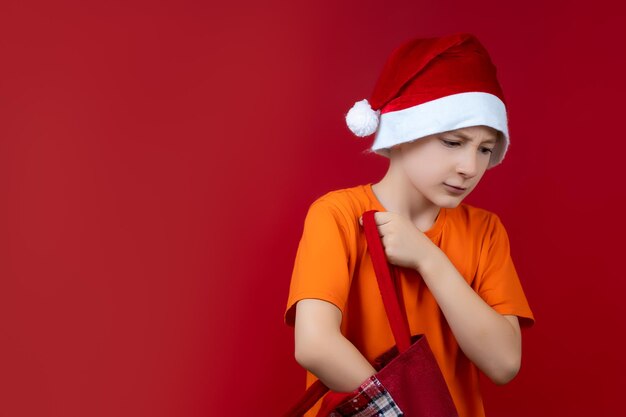 Ein Junge in einer Weihnachtsmütze auf rotem Grund mit einem Paket in der Hand