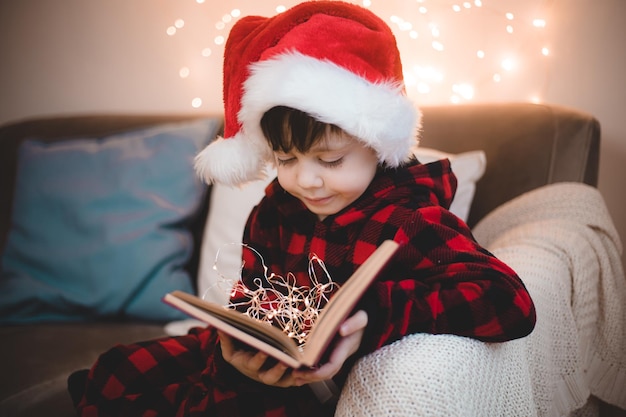 Ein Junge in einer Weihnachtsmütze liest ein Buch auf einem Lifestyle-Sofa Bücher lesen Neujahrsstimmung