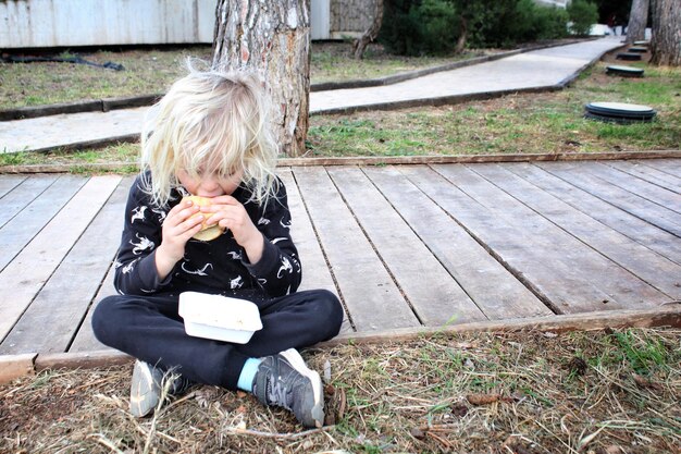 Foto ein junge in voller länge isst ein sandwich, während er im park sitzt