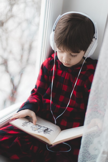 Ein Junge liest am Fenster ein Buch. Kinderbuch. Ein Artikel über Kinderfreizeit.