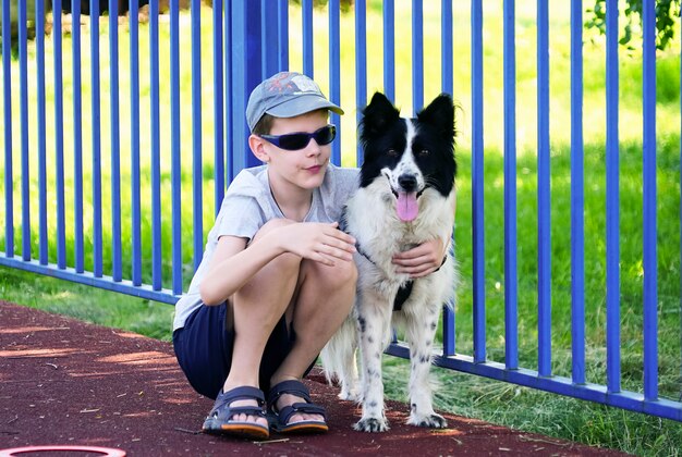 Ein Junge mit dunkler Brille sitzt und umarmt einen Hund.