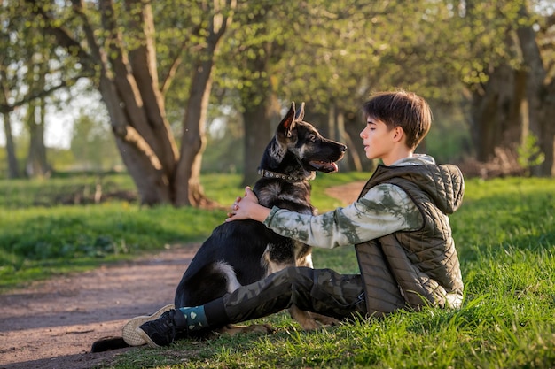 Ein Junge mit einem Hund spazieren im Park an einem sonnigen Frühlingsabend auf dem Gras sitzen Freundschaft von Mensch und Tier gesunder Lebensstil