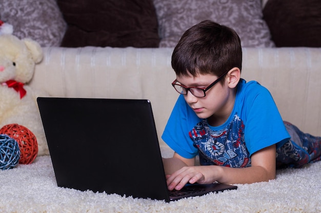 Ein Junge mit einem Laptop, der zu Hause auf dem Teppich auf dem Boden liegt Technologie Internet modernes Kommunikationskonzept