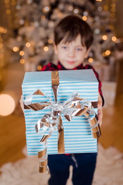 Ein Junge mit einem Neujahrsgeschenk unter dem Baum Lebensstil Festliche Dekoration des neuen Jahres und Weihnachten