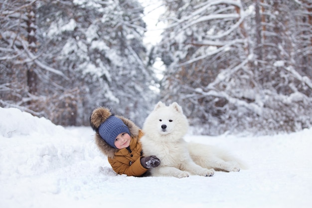 ein Junge mit einem weißen Hund, der im Schnee liegt