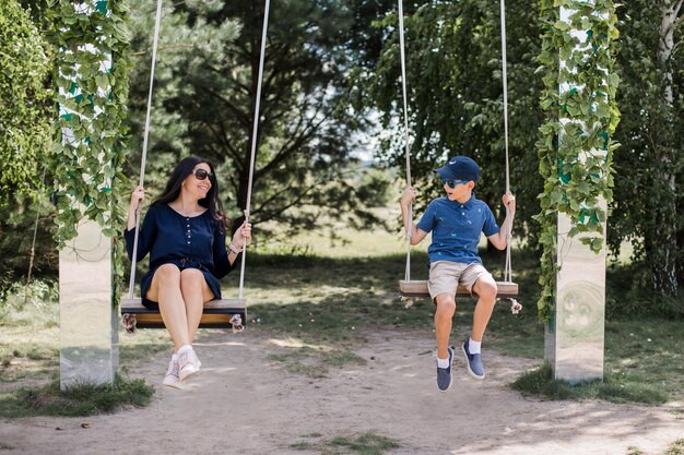 Ein Junge mit seiner Mutter reitet im Sommer auf einer Schaukel im Park