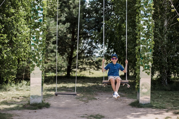 Ein Junge mit Sonnenbrille reitet im Sommer auf einer Schaukel im Park